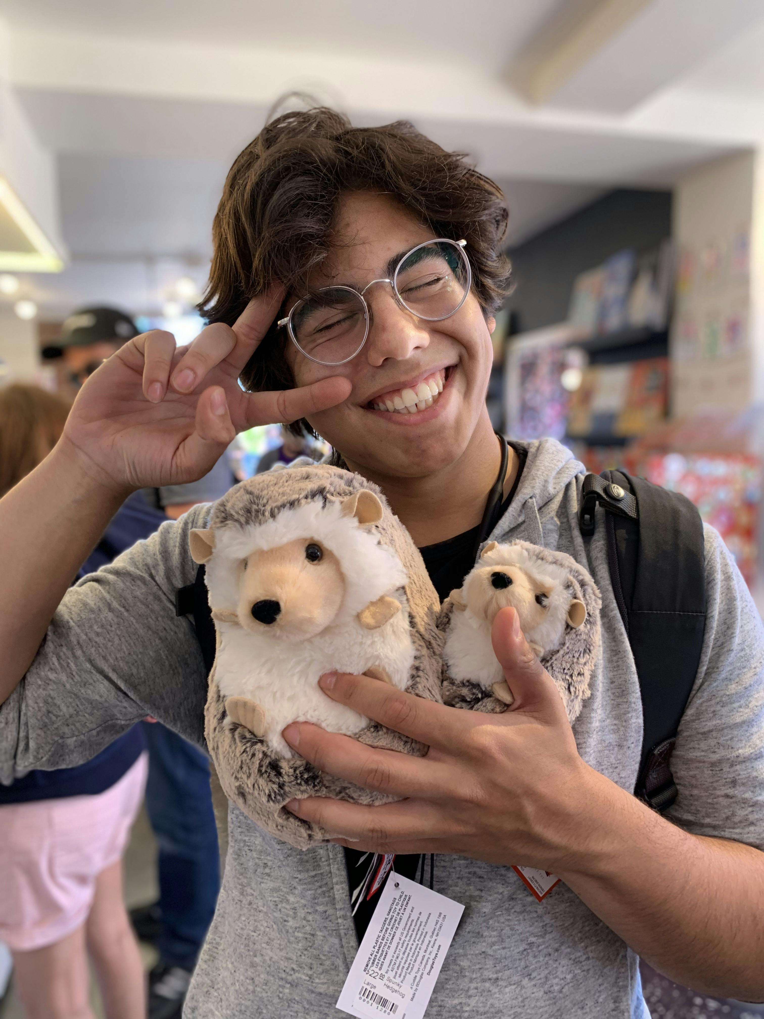 Photograph of Ziyad Edher in a stuffed animal store. He is holding a stuffed hedgehog plushie.